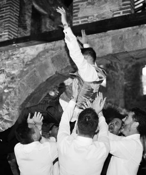 Grupo de personas levantando a un hombre en forma de celebración dentro de un edificio de piedra.