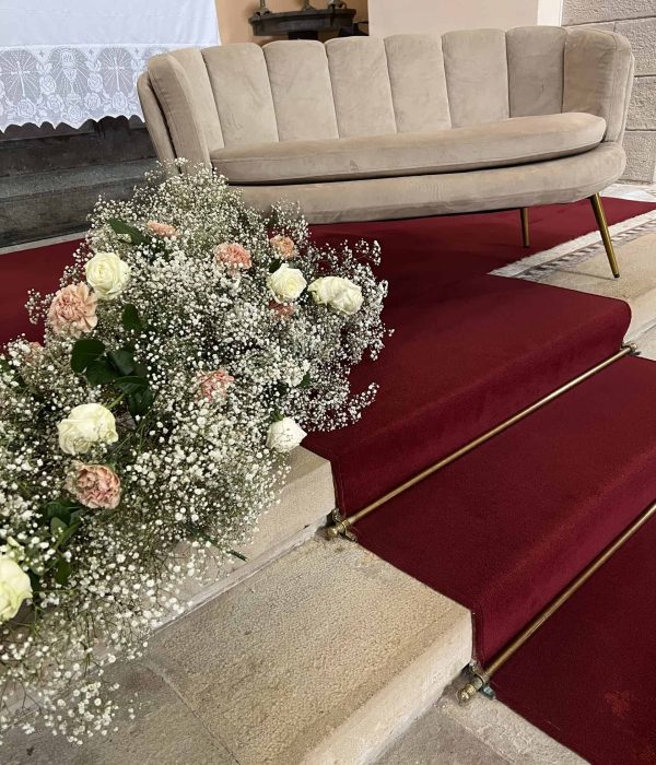 Un sofá beige se coloca sobre una plataforma alfombrada de color rojo con arreglos florales, incluidas flores blancas y rosas, en los escalones.