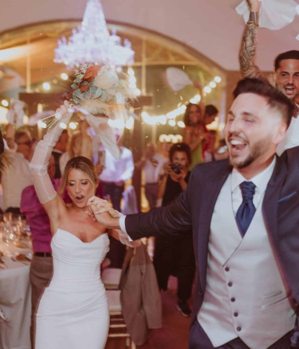 Novia y novio celebrando con alegría una recepción de boda con invitados y una decoración animada.